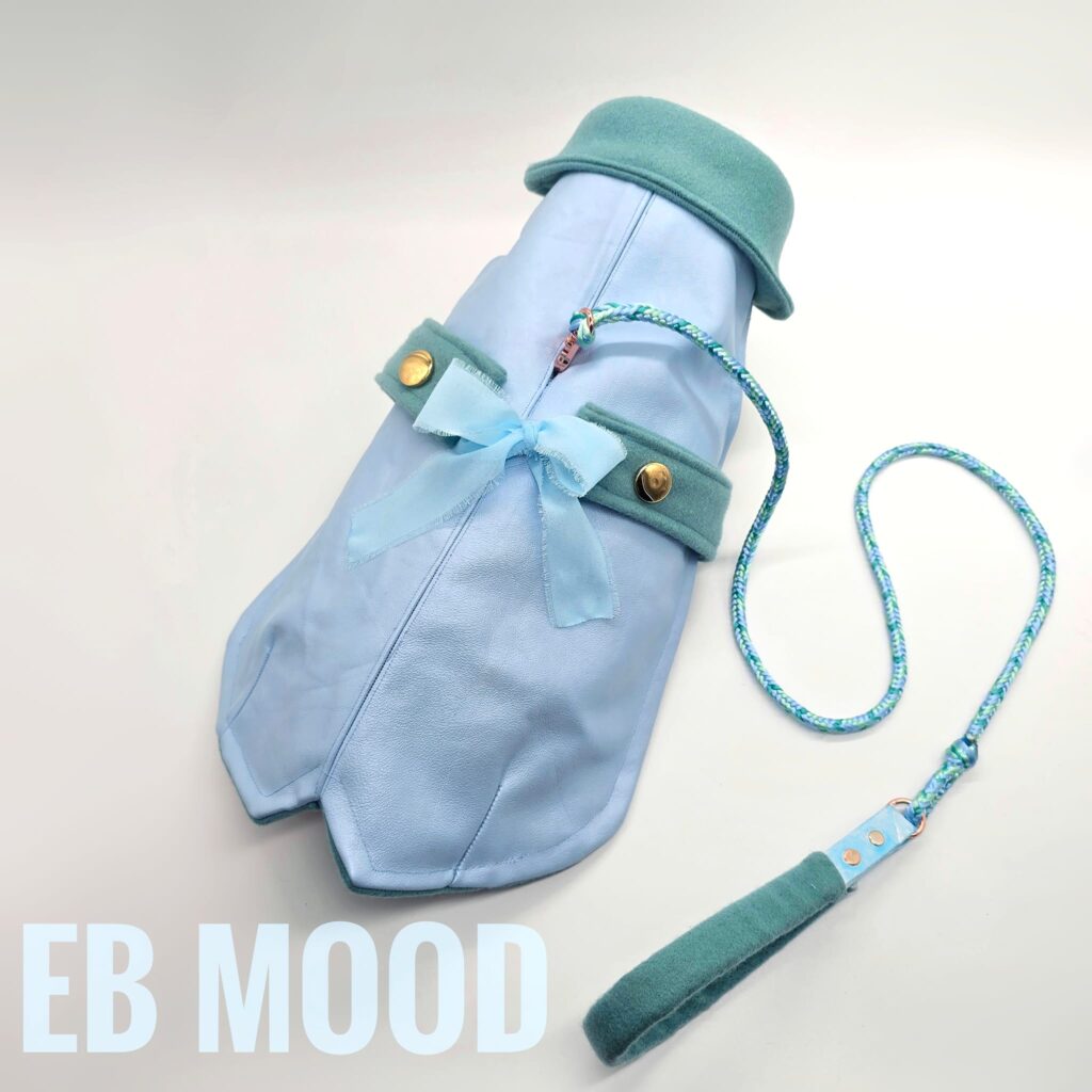 Cappotto EB MOOD linea SUPERIOR in versione ICE BLUE, realizzato su misura in vera pelle toscana e tessuto caldo, con dettagli in crepe di seta e bottoni dorati. Guinzaglio abbinato intrecciato a mano con maniglia rivestita nello stesso tessuto.